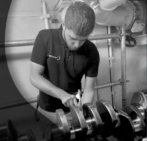 Motortec team member working on a specific Caterpillar engine part in black and white.