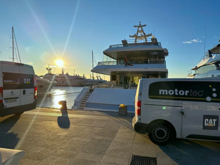 Motortec vans parked on a marina besides a berthed yacht - the sun is setting and it is a clear sky.
